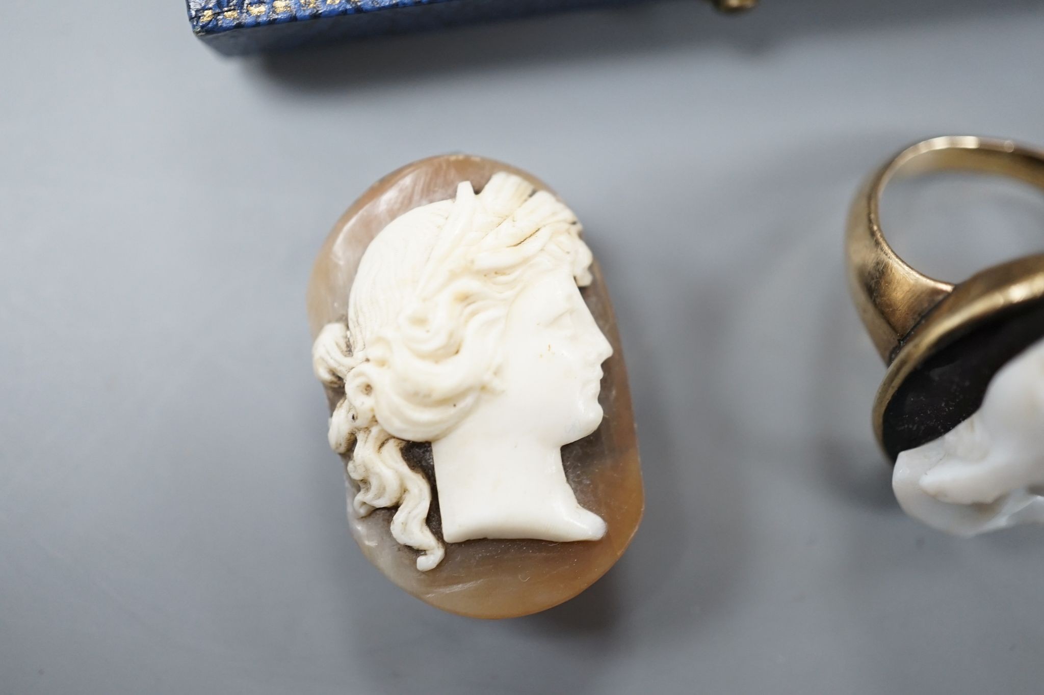 A yellow metal and hardstone set cameo ring, size J (a.f.), gross 6.9 grams, a pair of similar cameo shell ear clips and one other cameo shell mount.